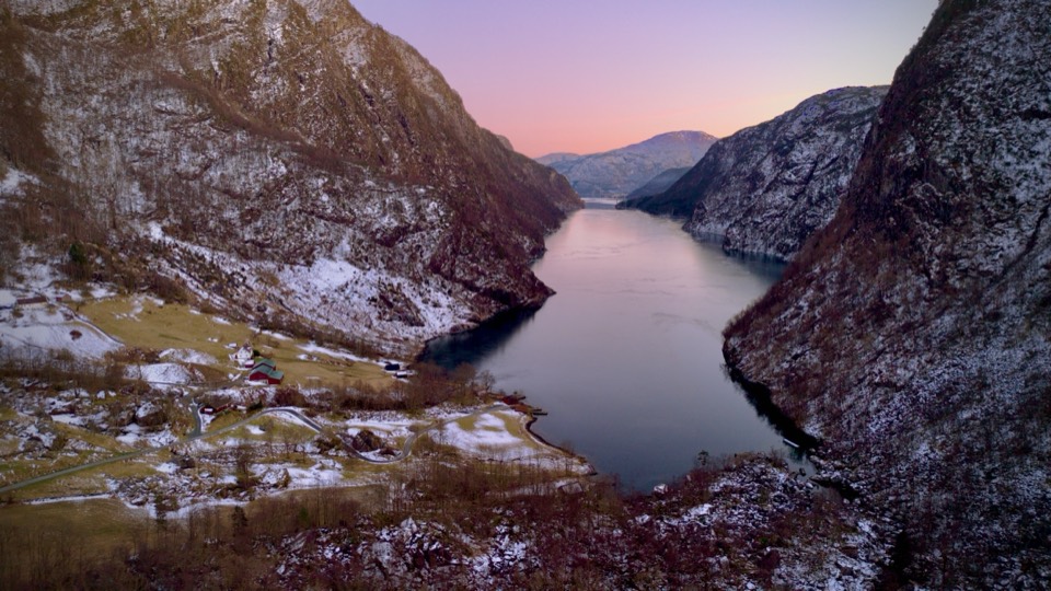 A fjord at dusk in winter, snow-dusted mountains under a pink sky
